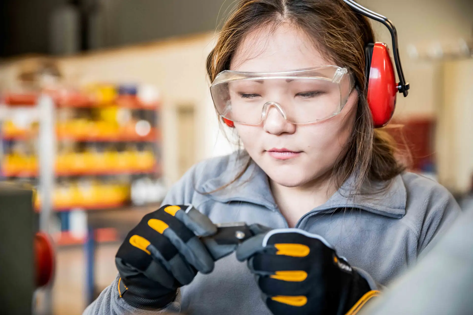 Frau mit Schutzbrille und Handschuhen, die in einer Werkstatt mit einem Werkzeug präzise arbeitet.